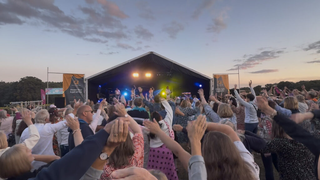 Crowd with phones raised in front of an outdoor stage at dusk