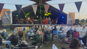 Audience sitting on the grass under bunting in front of the stage at Petal Fields