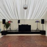Wedding marquee with DJ equipment hire in place: a DJ booth on a black riser, speakers either side and a mirror ball overhead