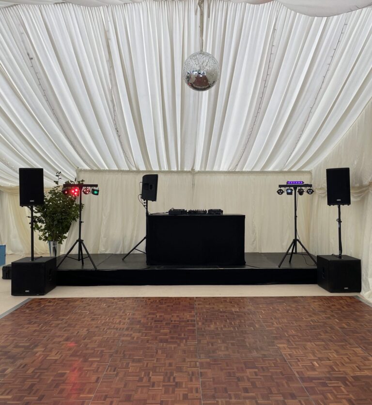 Wedding marquee with DJ equipment hire in place: a DJ booth on a black riser, speakers either side and a mirror ball overhead