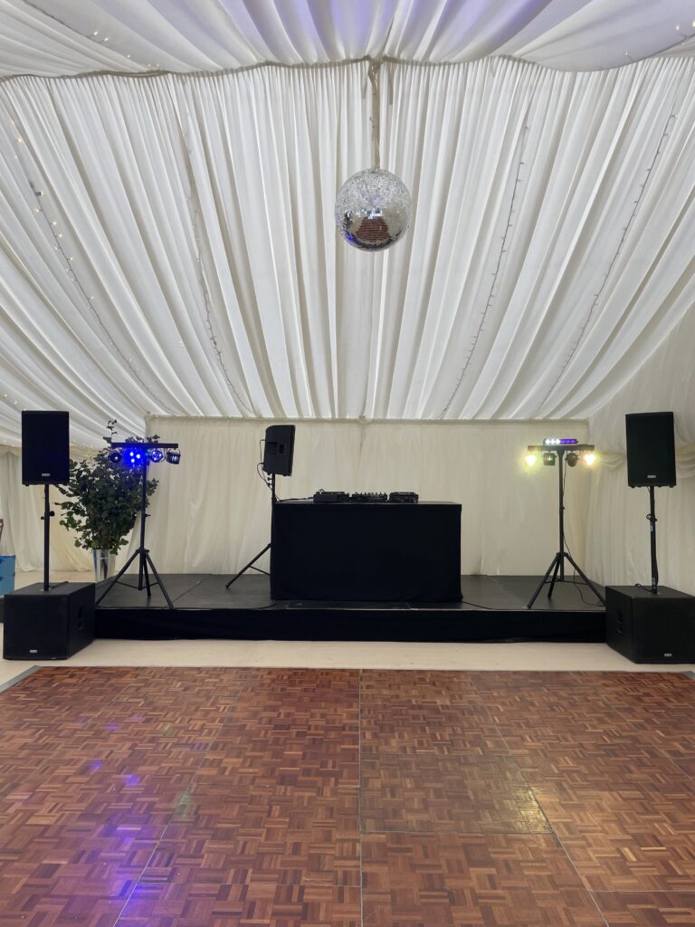 Marquee with white drapes, a dance floor and DJ equipment at the far end