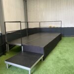 Black stage deck unit on green artificial grass inside a building