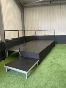 Black stage deck unit on green artificial grass inside a building