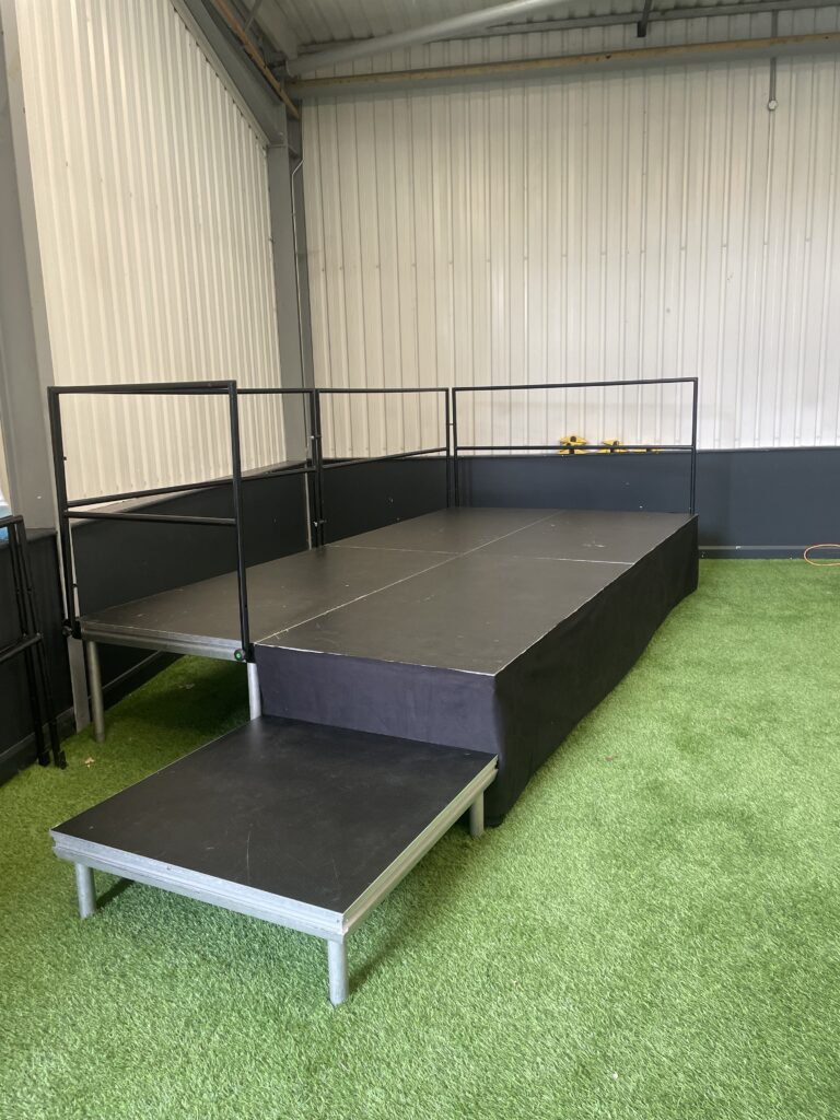 Black stage deck unit on green artificial grass inside a building