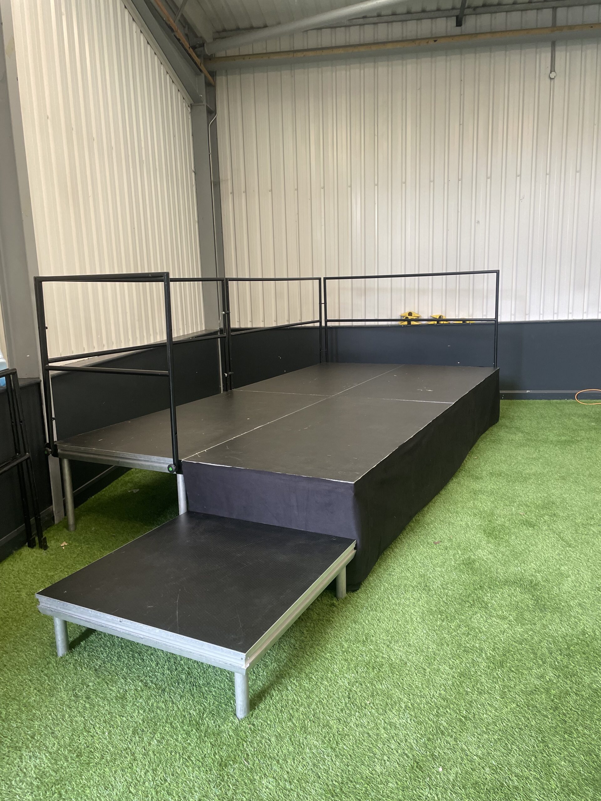Black stage deck unit on green artificial grass inside a building