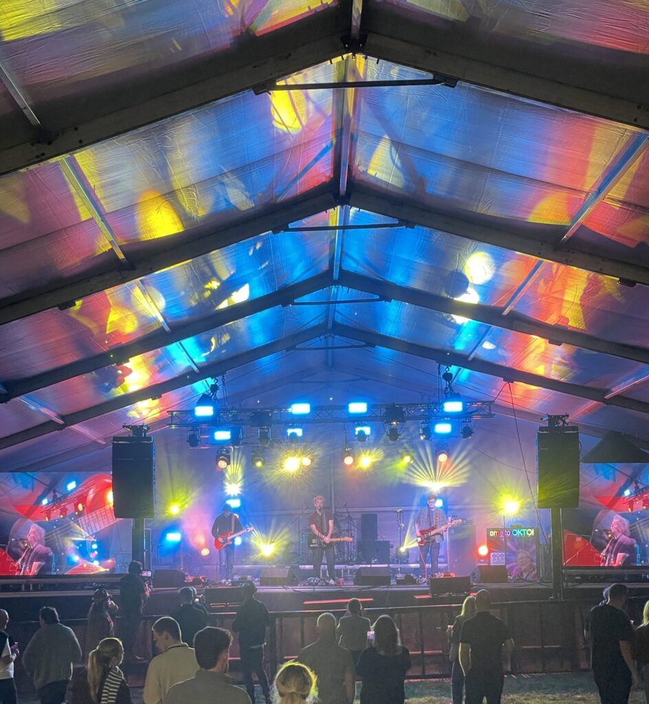Marquee lit in blue, pink and orange with the stage lighting and crowd in the foreground