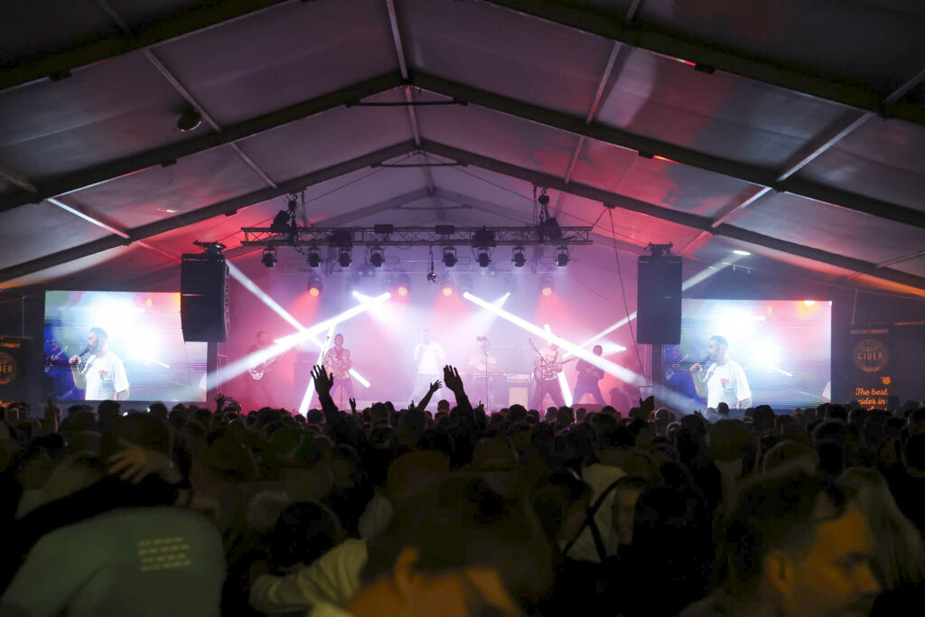 Marquee with a lighting rig beaming in pink and blue and LED screens either side of the stage