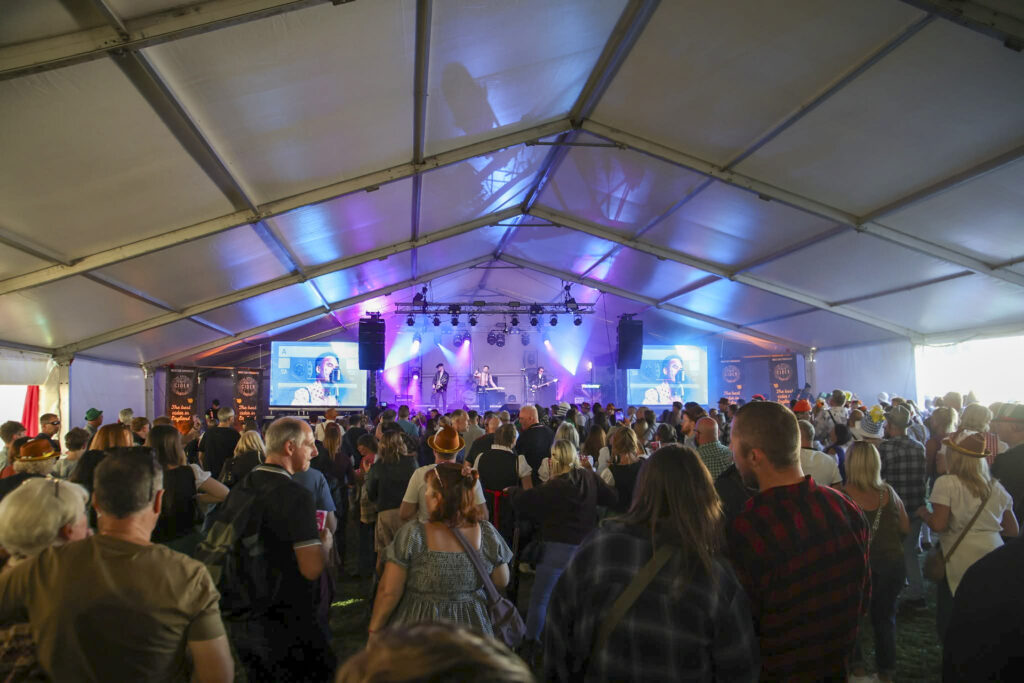 Large marquee with a stage and LED screens at the far end and a crowd throughout
