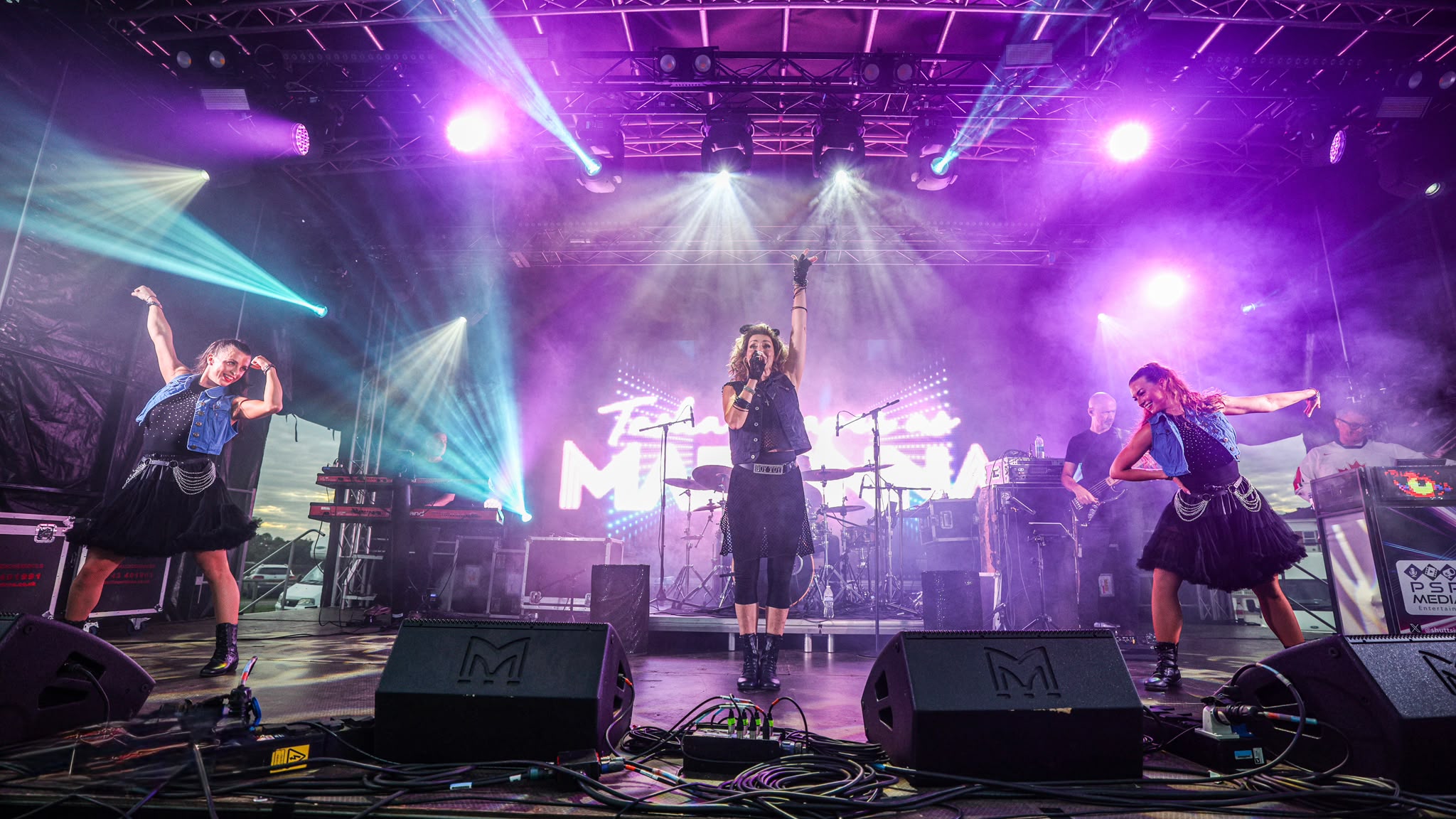 Band on stage at Avonstock 2026 lit in purple and magenta, with PA, lighting, video wall and live camera feeds by Pro Audio Services